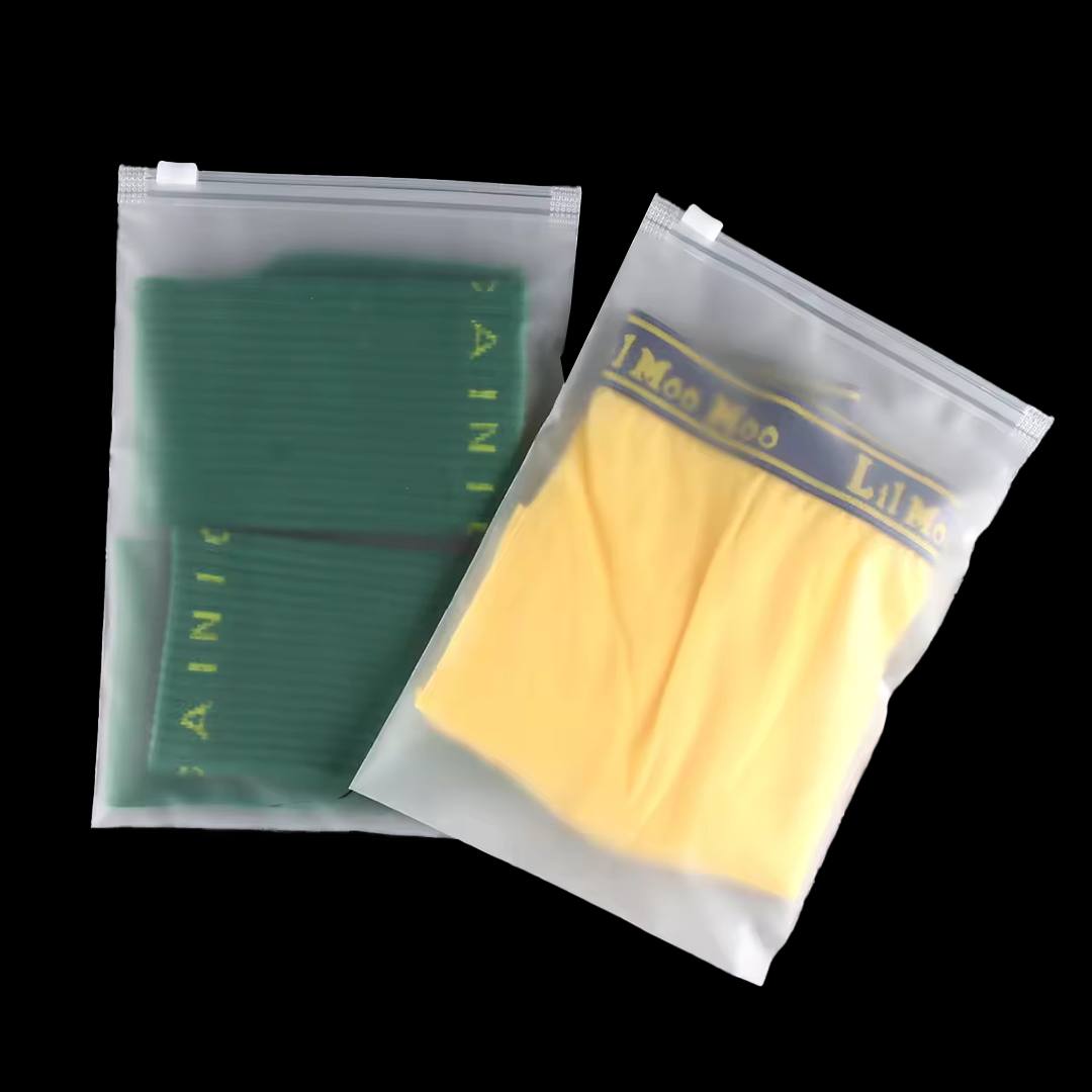 Two frosted zip bags holding folded knitwear in green and yellow, seen through the frosted film